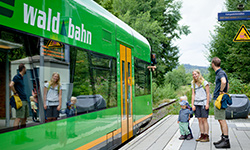 Ein Familie steht vor einem Waldbahn-Waggon